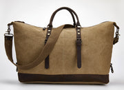 A large tan canvas duffel bag with dark brown leather handles, straps, and base trim, photographed on a clean white studio background.